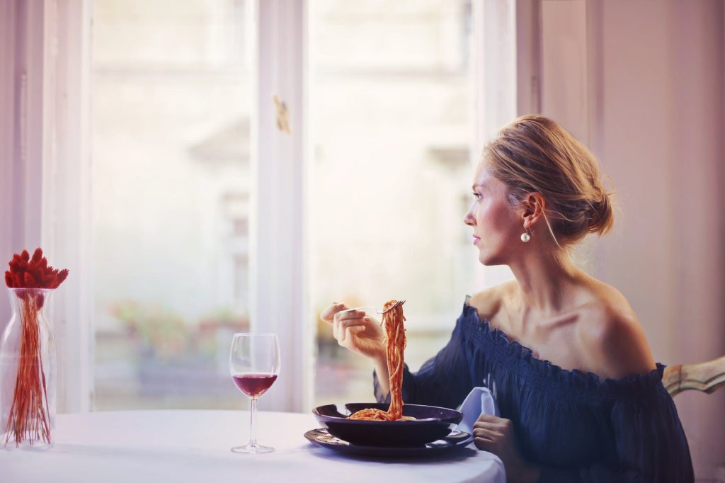 woman sitting on chair while eating pasta dish