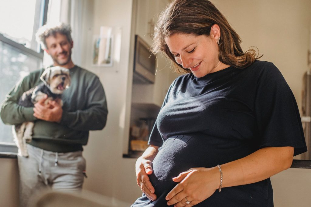 cheerful pregnant woman feeling child moving while husband with dog standing near