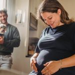 cheerful pregnant woman feeling child moving while husband with dog standing near