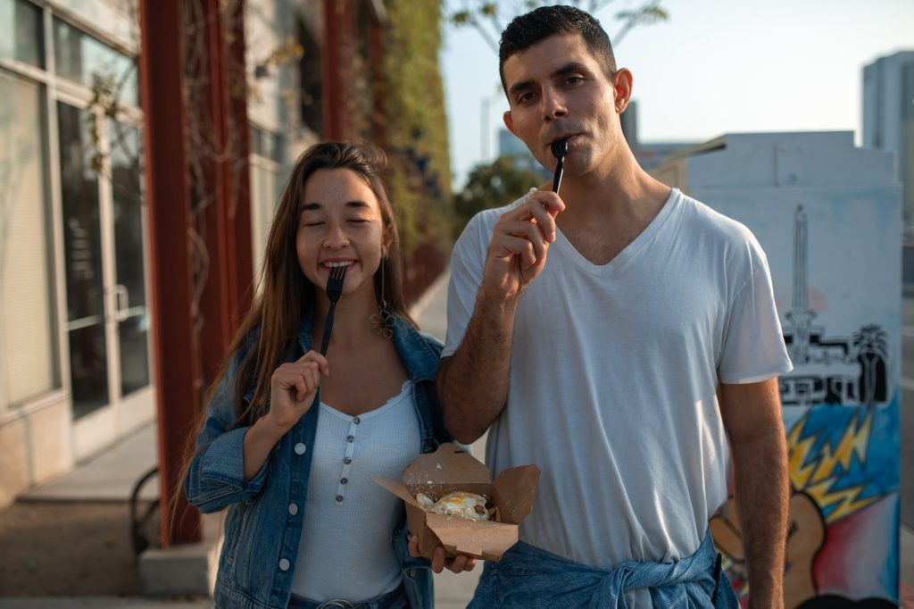 friends standing beside each other with disposable cutlery on their mouths