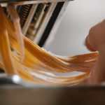 person cutting noodle with pasta machine