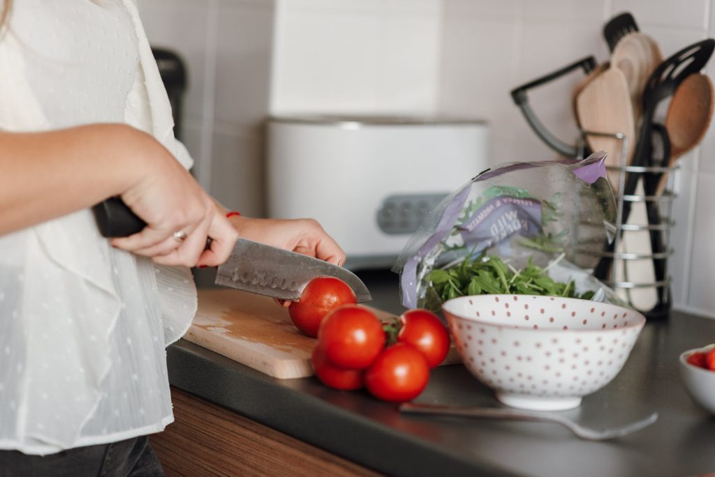 crop woman cutting tomatoes in kitchen