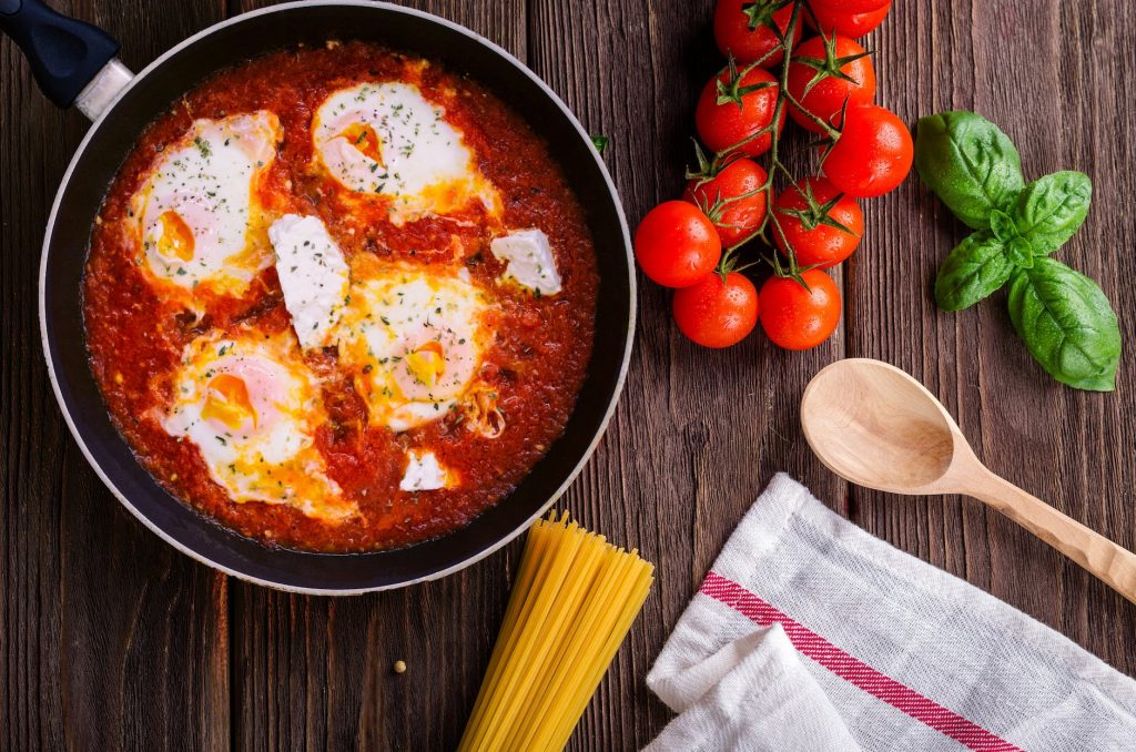 black frying pan with spaghetti sauce near brown wooden ladle and ripe tomatoes