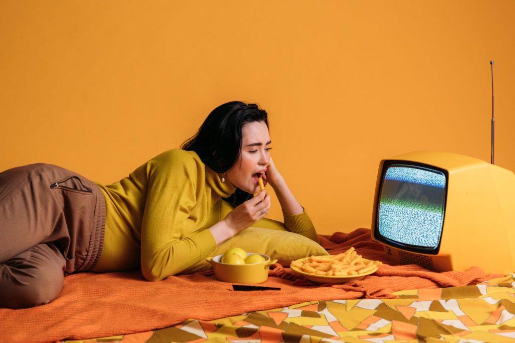 woman in yellow long sleeve shirt watching tv and eatinghi