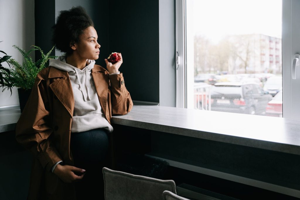 a pregnant woman eating apple while looking outside the window